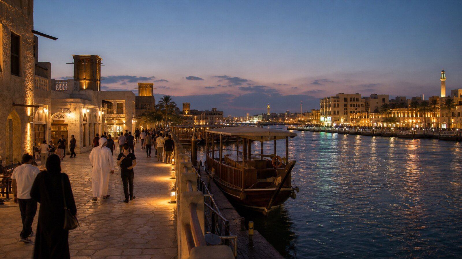 Historic Dubai Creek at blue hour with warm waterfront lighting, pedestrians and a traditional dhow